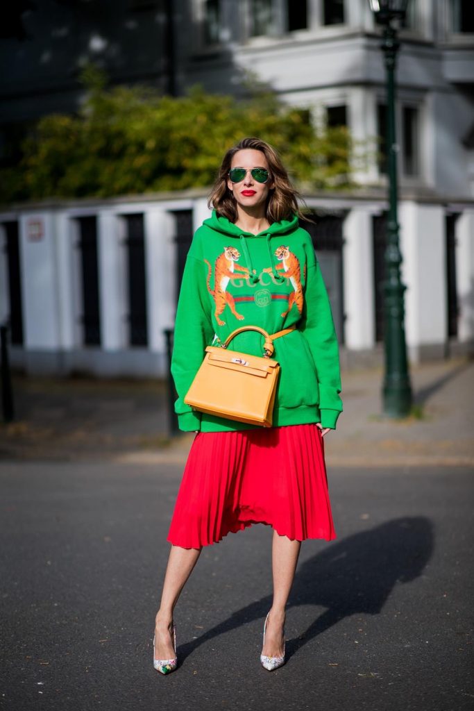Gucci, SET, Hermès, Christian Louboutin, Ray Ban Alexandra Lapp in a Hermès Kelly Look wearing a green tiger print Gucci logo hoodie, a red pleated skirt by SET, a Hermes Birkin 30 bag in orange, Pigalle Follies pumps by Christian Louboutin and green mirrored Ray Ban sunglasses on May 3, 2018 in Duesseldorf, Germany.