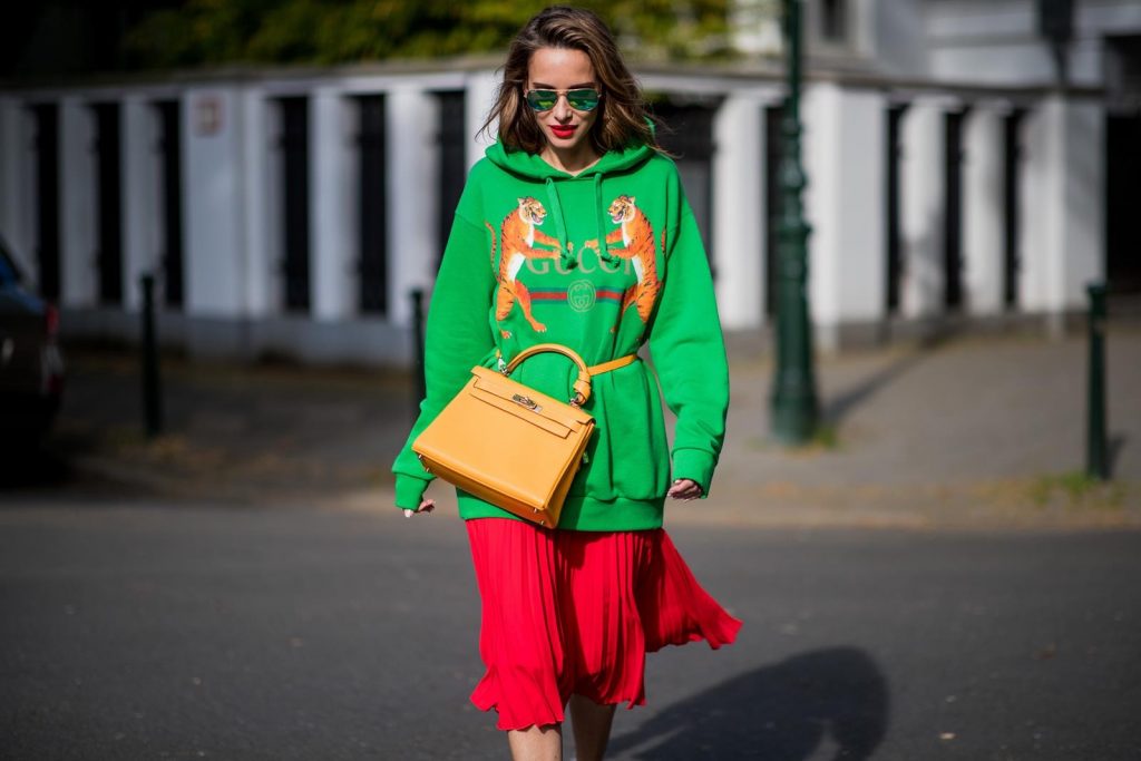 Gucci, SET, Hermès, Christian Louboutin, Ray Ban Alexandra Lapp in a Hermès Kelly Look wearing a green tiger print Gucci logo hoodie, a red pleated skirt by SET, a Hermes Birkin 30 bag in orange, Pigalle Follies pumps by Christian Louboutin and green mirrored Ray Ban sunglasses on May 3, 2018 in Duesseldorf, Germany.