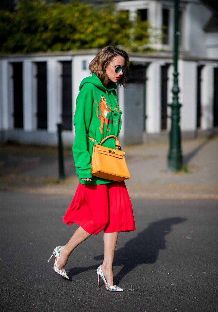 Gucci, SET, Hermès, Christian Louboutin, Ray Ban Alexandra Lapp in a Hermès Kelly Look wearing a green tiger print Gucci logo hoodie, a red pleated skirt by SET, a Hermes Birkin 30 bag in orange, Pigalle Follies pumps by Christian Louboutin and green mirrored Ray Ban sunglasses on May 3, 2018 in Duesseldorf, Germany.