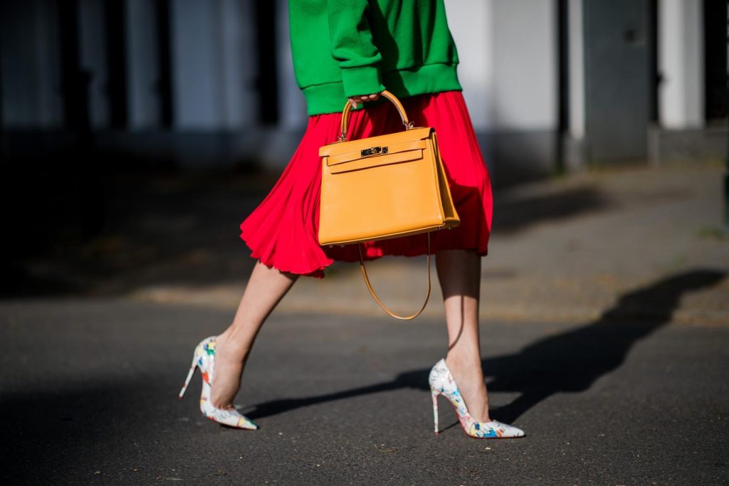 Gucci, SET, Hermès, Christian Louboutin, Ray Ban Alexandra Lapp in a Hermès Kelly Look wearing a green tiger print Gucci logo hoodie, a red pleated skirt by SET, a Hermes Birkin 30 bag in orange, Pigalle Follies pumps by Christian Louboutin and green mirrored Ray Ban sunglasses on May 3, 2018 in Duesseldorf, Germany.