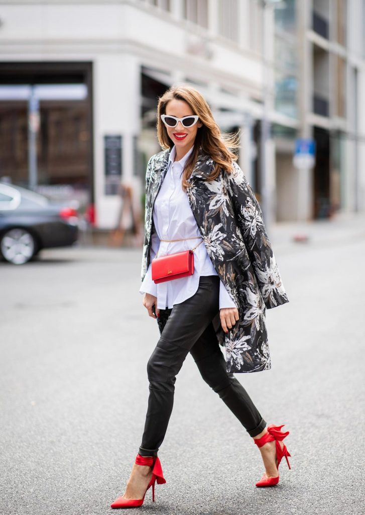 Alexandra Lapp in Floral Blazer Coat Look wearing a long blazer jacket with floral prints in green, white and gold tones from Steffen Schraut, a white long shirt and slim leather pants in black with stitches around the knee from Steffen Schraut, the red Douce Du Desert 100 Flamenco Satin sandals from Christian Louboutin with a long ribbon tied around the ankle, a red little clutch from Christian Louboutin around the waist and white Saint Laurent New Wave Lily sunglasses is seen during the Berlin Fashion Week July 2018 on July 6, 2018 in Berlin, Germany.