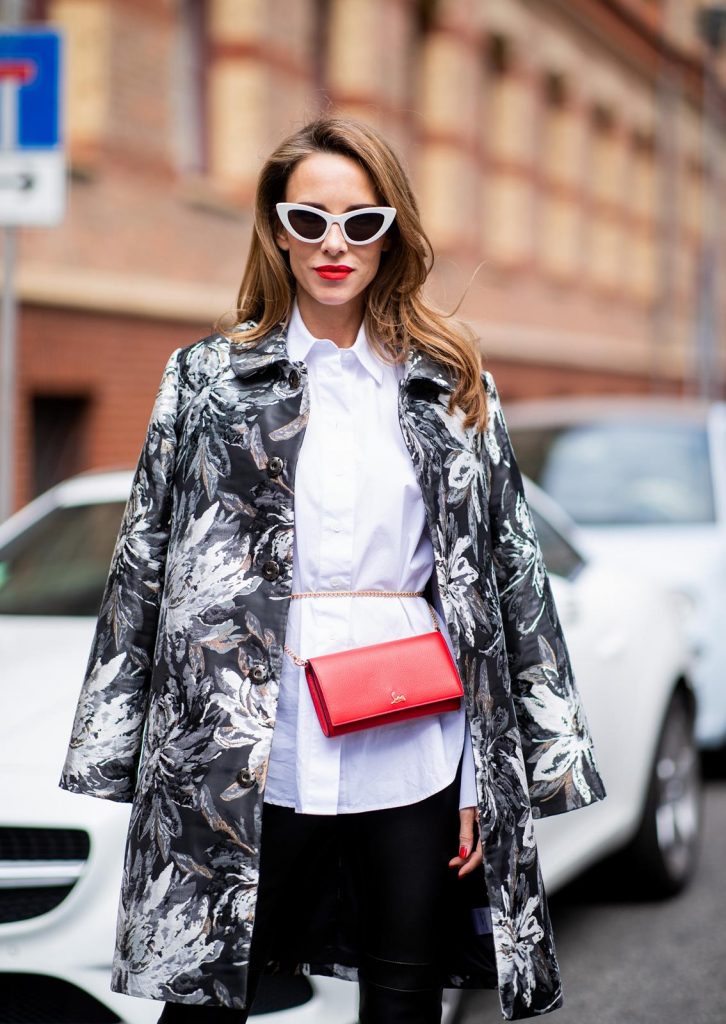 Alexandra Lapp in Floral Blazer Coat Look wearing a long blazer jacket with floral prints in green, white and gold tones from Steffen Schraut, a white long shirt and slim leather pants in black with stitches around the knee from Steffen Schraut, the red Douce Du Desert 100 Flamenco Satin sandals from Christian Louboutin with a long ribbon tied around the ankle, a red little clutch from Christian Louboutin around the waist and white Saint Laurent New Wave Lily sunglasses is seen during the Berlin Fashion Week July 2018 on July 6, 2018 in Berlin, Germany.