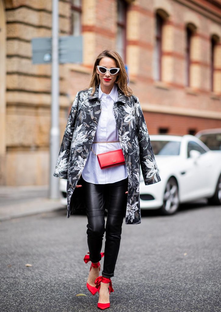 Alexandra Lapp in Floral Blazer Coat Look wearing a long blazer jacket with floral prints in green, white and gold tones from Steffen Schraut, a white long shirt and slim leather pants in black with stitches around the knee from Steffen Schraut, the red Douce Du Desert 100 Flamenco Satin sandals from Christian Louboutin with a long ribbon tied around the ankle, a red little clutch from Christian Louboutin around the waist and white Saint Laurent New Wave Lily sunglasses is seen during the Berlin Fashion Week July 2018 on July 6, 2018 in Berlin, Germany.