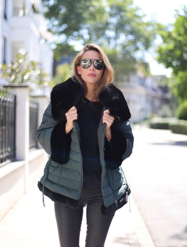Airfield, SET, James Perse, Saint Laurent, Hermès, Céline Model and Blogger Alexandra Lapp in a Faux Fur Jacket Look wearing a black down jacket with faux fur by Airfield, black leather pants by SET, black T-Shirt by James Perse, dark green leather overknee boots by Saint Laurent, black Kelly bag by Hermès and black Audrey sunglasses from Céline.