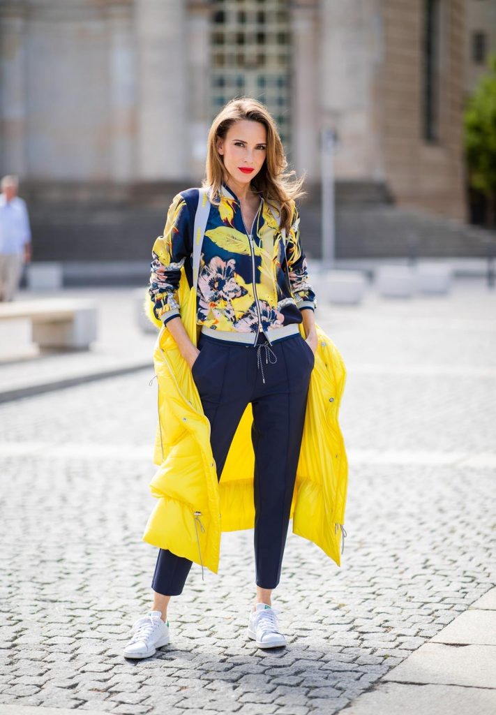 Alexandra Lapp in a Floral Jacket | Yellow Coat Look is seen wearing a blouson jacket with floral print, blue drawstring pants and a bright yellow duffle coat with a yellow fur hood from Airfield, Céline sunglasses in black, white Stan Smith Adidas sneakers with green details during the Berlin Fashion Week July 2018 on July 6, 2018 in Berlin, Germany.
