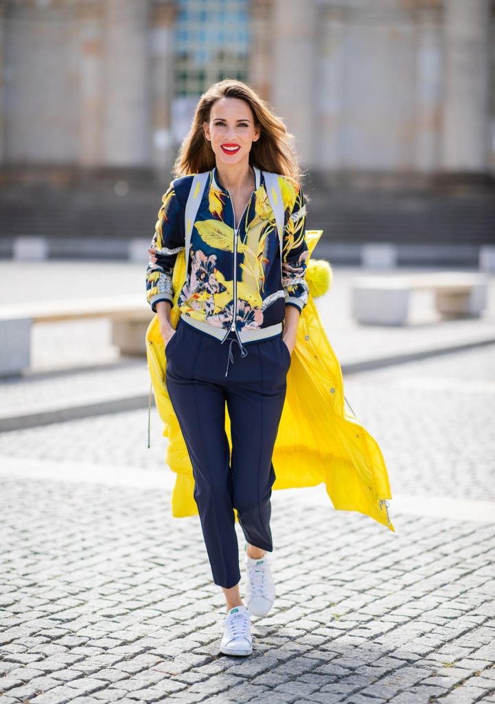 Alexandra Lapp in a Floral Jacket | Yellow Coat Look is seen wearing a blouson jacket with floral print, blue drawstring pants and a bright yellow duffle coat with a yellow fur hood from Airfield, Céline sunglasses in black, white Stan Smith Adidas sneakers with green details during the Berlin Fashion Week July 2018 on July 6, 2018 in Berlin, Germany.