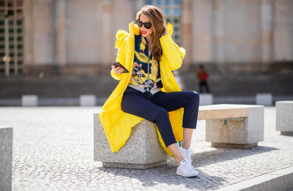 Alexandra Lapp in a Floral Jacket | Yellow Coat Look is seen wearing a blouson jacket with floral print, blue drawstring pants and a bright yellow duffle coat with a yellow fur hood from Airfield, Céline sunglasses in black, white Stan Smith Adidas sneakers with green details during the Berlin Fashion Week July 2018 on July 6, 2018 in Berlin, Germany.