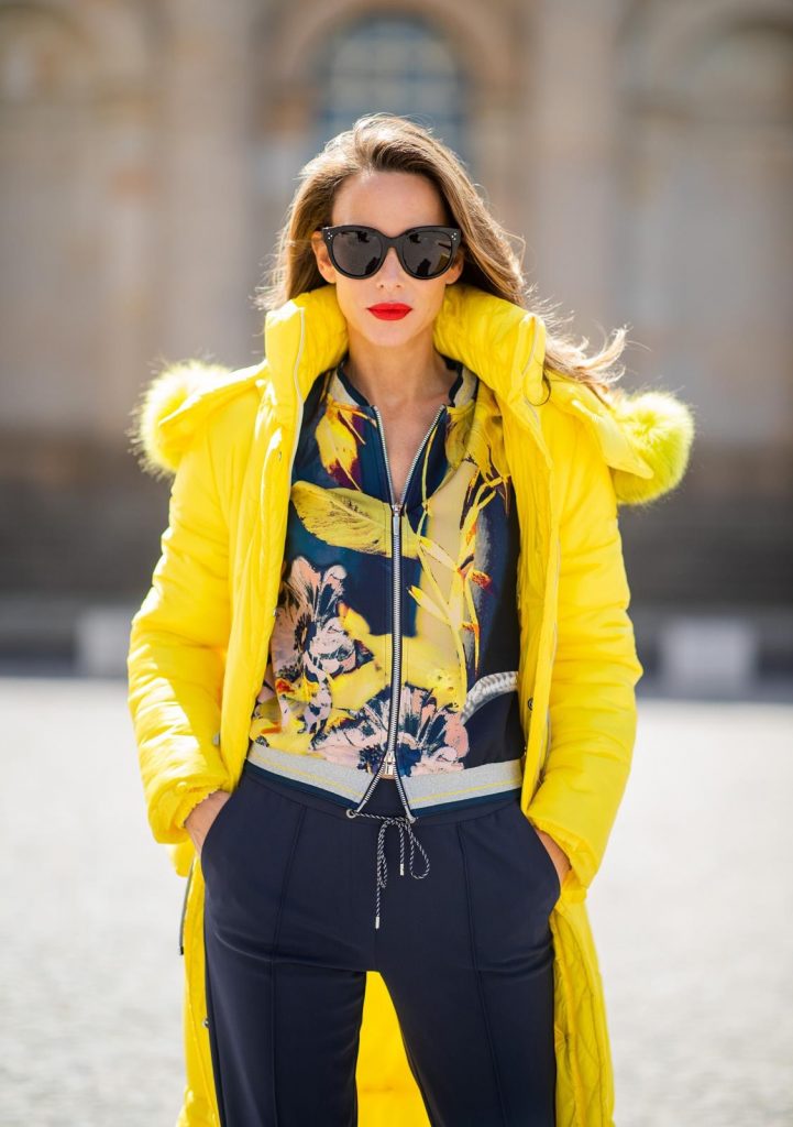 Alexandra Lapp in a Floral Jacket | Yellow Coat Look is seen wearing a blouson jacket with floral print, blue drawstring pants and a bright yellow duffle coat with a yellow fur hood from Airfield, Céline sunglasses in black, white Stan Smith Adidas sneakers with green details during the Berlin Fashion Week July 2018 on July 6, 2018 in Berlin, Germany.