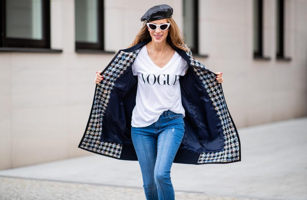 Alexandra Lapp wearing an oversized college jacket look with an oversized checkered college jacket from Steffen Schraut, stirrup denim pants from Steffen Schraut, a white V-neck t-shirt saying Vogue on the front from Your&Self, High Heel Sandals Sandale Du Desert in denim blue with a printed satin bow from Christian Louboutin, a silver Chanel handbag, white cat-eye sunglasses from YSL - Saint Laurent and Eugenia Kim leather basque Cher Barett on July 13, 2018 in Berlin, Germany.