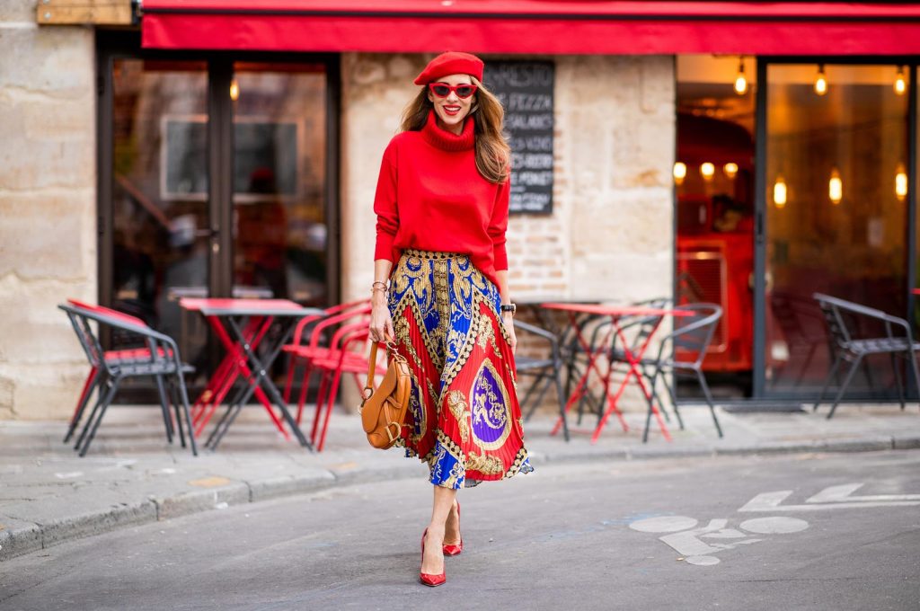 Versace, Falconeri, Dior, Gianvito Rossi, Zara, Céline Alexandra Lapp seen in a Versace Skirt Look wearing a pleated printed midi skirt from Versace, a long red cashmere turtle neck pullover from Falconeri, a vintage Dior saddle bag in cognac, red pumps from Gianvito Rossi, a beret cap in red from Zara, red cat-eye shaped sunglasses from Celine during Paris Fashion Week Womenswear Spring/Summer 2019 on September 29, 2018 in Paris, France.