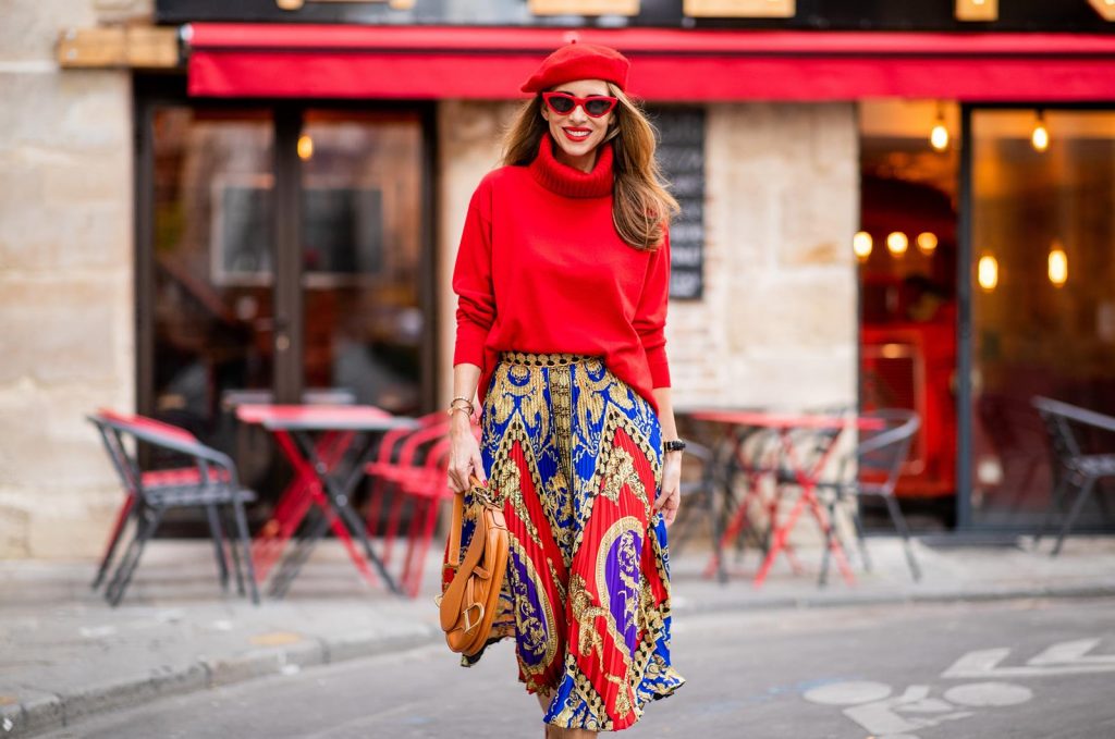 Versace, Falconeri, Dior, Gianvito Rossi, Zara, Céline Alexandra Lapp seen in a Versace Skirt Look wearing a pleated printed midi skirt from Versace, a long red cashmere turtle neck pullover from Falconeri, a vintage Dior saddle bag in cognac, red pumps from Gianvito Rossi, a beret cap in red from Zara, red cat-eye shaped sunglasses from Celine during Paris Fashion Week Womenswear Spring/Summer 2019 on September 29, 2018 in Paris, France.