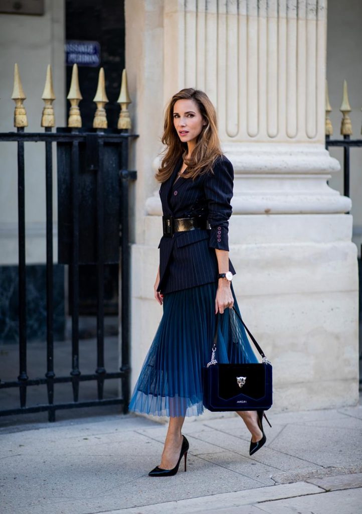 Alexandra Lapp in an All Blue Everything Look wearing a blue pleated skirt, navy striped blazer with belt and blue velvet bag all by Marc Cain, black heels from Christian Louboutin, a black lacquer waist belt by Dolce & Gabbana and black Audrey sunglasses by Céline seen during Paris Fashion Week Womenswear Spring/Summer 2019 on September 25, 2018 in Paris, France.