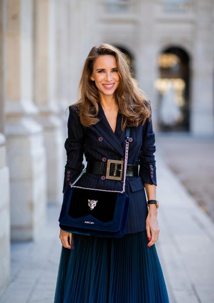 Alexandra Lapp in an All Blue Everything Look wearing a blue pleated skirt, navy striped blazer with belt and blue velvet bag all by Marc Cain, black heels from Christian Louboutin, a black lacquer waist belt by Dolce & Gabbana and black Audrey sunglasses by Céline seen during Paris Fashion Week Womenswear Spring/Summer 2019 on September 25, 2018 in Paris, France.