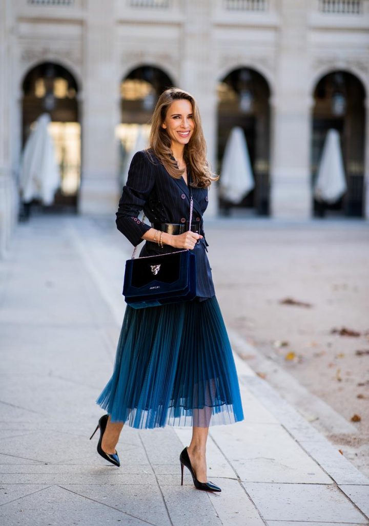 Alexandra Lapp in an All Blue Everything Look wearing a blue pleated skirt, navy striped blazer with belt and blue velvet bag all by Marc Cain, black heels from Christian Louboutin, a black lacquer waist belt by Dolce & Gabbana and black Audrey sunglasses by Céline seen during Paris Fashion Week Womenswear Spring/Summer 2019 on September 25, 2018 in Paris, France.
