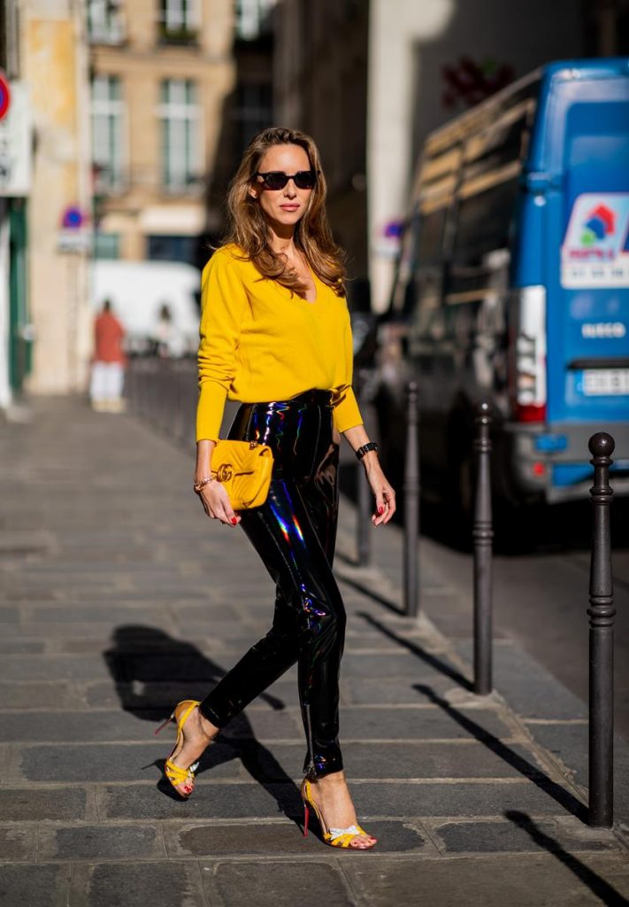 Alexandra Lapp in a Vinyl Pants Look wearing black zipped patent leather trousers from Balmain, a yellow v-neck knit jumper by Allude, shiny black down jacket by Ahirain, yellow Gucci Matelasse GG bag, yellow white Metrisandal open toe sandals with tape-style straps by Christian Louboutin and cat-eye shaped Isabella Sunglasses by illesteva during Paris Fashion Week Womenswear Spring/Summer 2019 on September 27, 2018 in Paris, France.