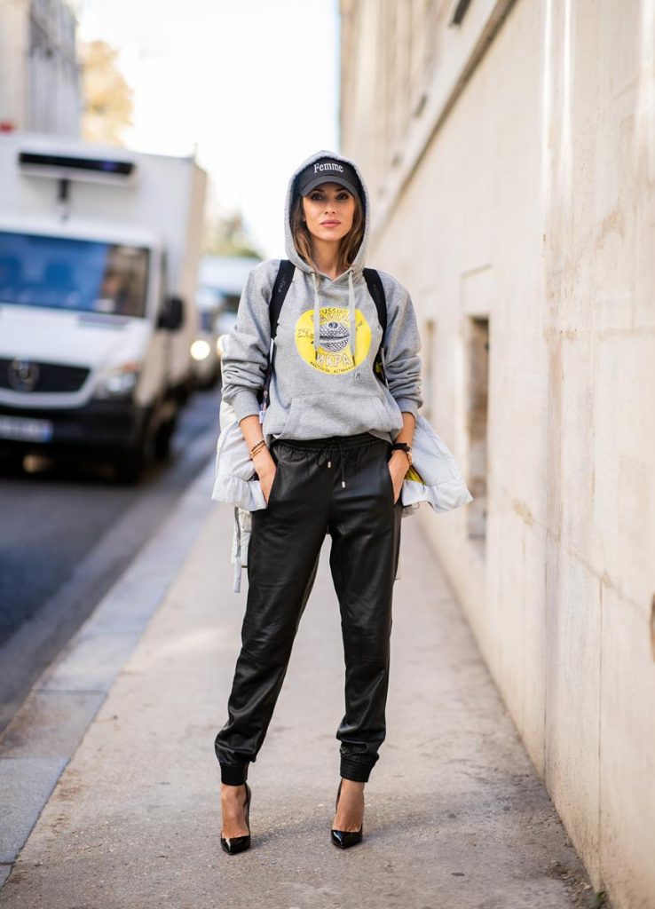 Alexandra Lapp in a Light Down Jacket Look wearing a light grey, fitted down jacket with inner carriers by Airfield, a handmade grey Hoodie with hand-painted print by Wodka Ogurez, black leather pants by SET, black Femme baseball cap from Balenciaga and black patent leather pumps by Christian Louboutin during Paris Fashion Week Womenswear Spring/Summer 2019 on September 24, 2018 in Paris, France.