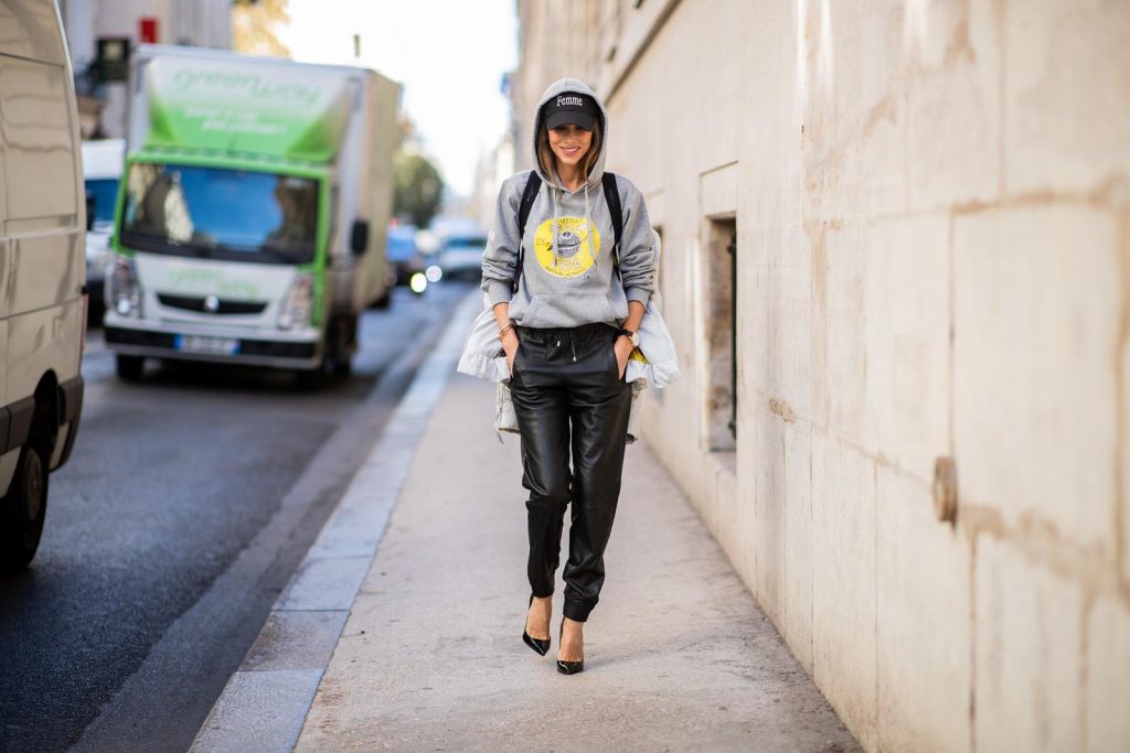 Alexandra Lapp in a Light Down Jacket Look wearing a light grey, fitted down jacket with inner carriers by Airfield, a handmade grey Hoodie with hand-painted print by Wodka Ogurez, black leather pants by SET, black Femme baseball cap from Balenciaga and black patent leather pumps by Christian Louboutin during Paris Fashion Week Womenswear Spring/Summer 2019 on September 24, 2018 in Paris, France.