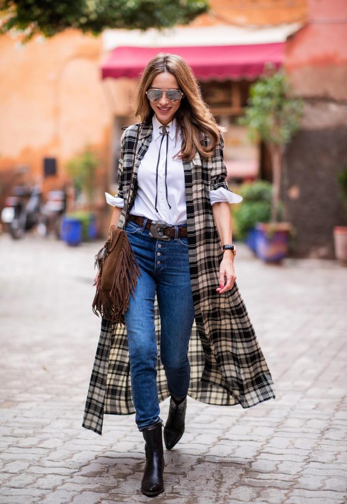 Polo Ralph Lauren, Loro Piana, Adriano Goldschmied, Saint Laurent, Isabel Marant, Christian Dior, Chanel, Givenchy Alexandra Lapp in a Cowboy Style Look wearing a long checkered shirt dress from Polo Ralph Lauren, a white shirt from Loro Piana, light blue denims from Adriano Goldschmied, a brown suede leather bag with long fringes and a buckle with feathers from Saint Laurent, a black leather belt with white stitches from Isabel Marant, black Cowboy boots from Christian Dior, a silver Chanel brooch and mirrored sunglasses from Givenchy on November 25, 2018 in Marrakech, Morocco.