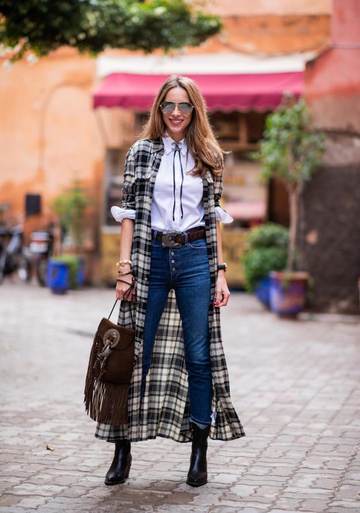 Polo Ralph Lauren, Loro Piana, Adriano Goldschmied, Saint Laurent, Isabel Marant, Christian Dior, Chanel, Givenchy Alexandra Lapp in a Cowboy Style Look wearing a long checkered shirt dress from Polo Ralph Lauren, a white shirt from Loro Piana, light blue denims from Adriano Goldschmied, a brown suede leather bag with long fringes and a buckle with feathers from Saint Laurent, a black leather belt with white stitches from Isabel Marant, black Cowboy boots from Christian Dior, a silver Chanel brooch and mirrored sunglasses from Givenchy on November 25, 2018 in Marrakech, Morocco.