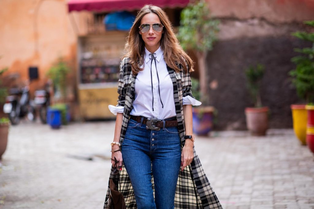 Polo Ralph Lauren, Loro Piana, Adriano Goldschmied, Saint Laurent, Isabel Marant, Christian Dior, Chanel, Givenchy Alexandra Lapp in a Cowboy Style Look wearing a long checkered shirt dress from Polo Ralph Lauren, a white shirt from Loro Piana, light blue denims from Adriano Goldschmied, a brown suede leather bag with long fringes and a buckle with feathers from Saint Laurent, a black leather belt with white stitches from Isabel Marant, black Cowboy boots from Christian Dior, a silver Chanel brooch and mirrored sunglasses from Givenchy on November 25, 2018 in Marrakech, Morocco.