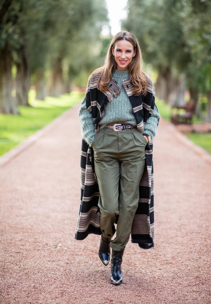 Alexandra Lapp wearing a wool cape look with the long Huan fringed striped wool cape from Isabel Marant, chunky-knit wool jumper by H&M in dusky green, utility trousers in khaki green by H&M, black leather belt with white stitches from Isabel Marant, black Cowboy boots with a silver tip from Isabel Marant, black Kelly bag from Hermès and oversized golden earrings from H&M on November 25, 2018 in Marrakech, Morocco. (Photo by Christian Vierig/Getty Images)