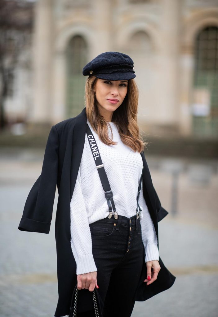Alexandra Lapp in A Chanel Rain Boots look, wearing a soft long blazer by Steffen Schraut, over a white chunky knit sweater by H&M, black skinny pants with golden buttons by Veronica Beard, styled with Chanel logo suspenders and Chanel rain boots, the Chanel Le boy bag, a Chanel tweed baker boy cap and a transparent umbrella by Mirviory during the Berlin Fashion Week Autumn/Winter 2019 on January 15, 2019 in Berlin, Germany. (Photo by Christian Vierig/Getty Images)