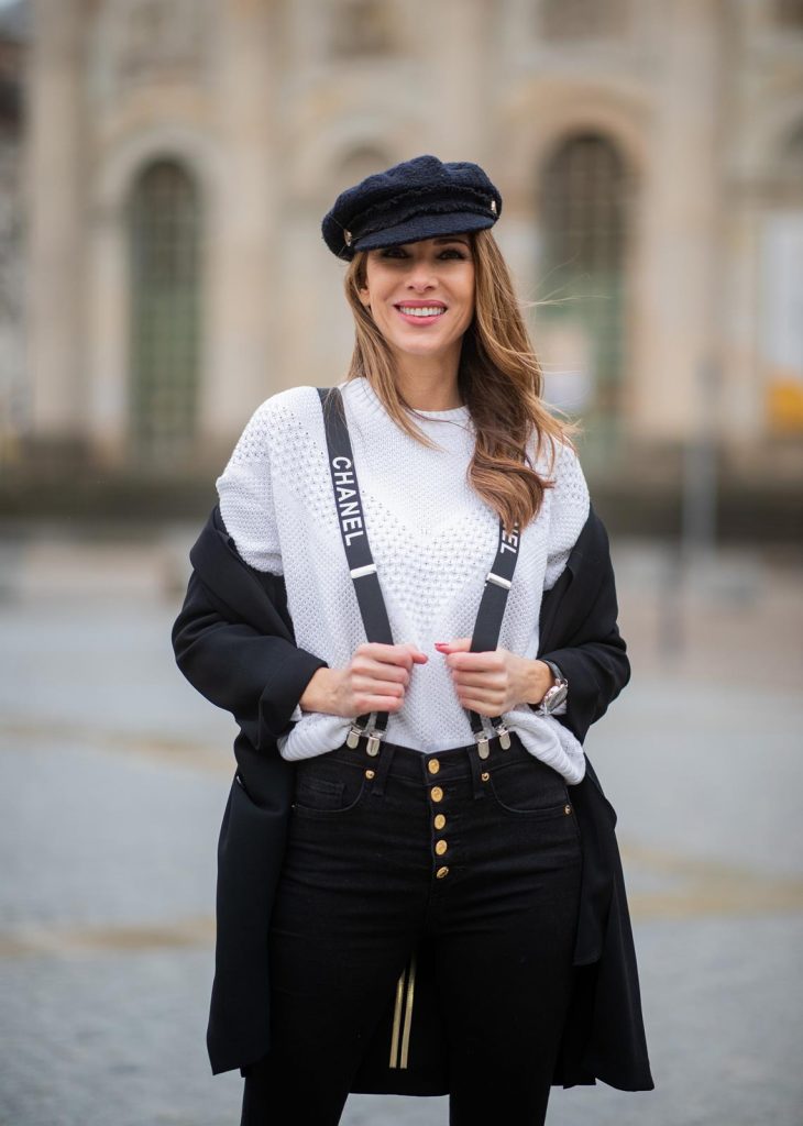 Alexandra Lapp in A Chanel Rain Boots look, wearing a soft long blazer by Steffen Schraut, over a white chunky knit sweater by H&M, black skinny pants with golden buttons by Veronica Beard, styled with Chanel logo suspenders and Chanel rain boots, the Chanel Le boy bag, a Chanel tweed baker boy cap and a transparent umbrella by Mirviory during the Berlin Fashion Week Autumn/Winter 2019 on January 15, 2019 in Berlin, Germany. (Photo by Christian Vierig/Getty Images)