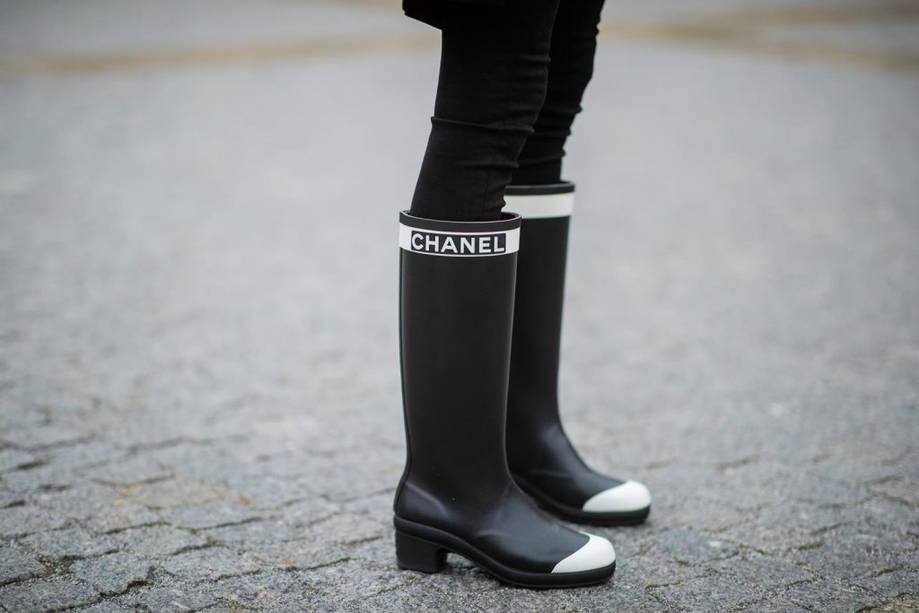 Alexandra Lapp in A Chanel Rain Boots look, wearing a soft long blazer by Steffen Schraut, over a white chunky knit sweater by H&M, black skinny pants with golden buttons by Veronica Beard, styled with Chanel logo suspenders and Chanel rain boots, the Chanel Le boy bag, a Chanel tweed baker boy cap and a transparent umbrella by Mirviory during the Berlin Fashion Week Autumn/Winter 2019 on January 15, 2019 in Berlin, Germany. (Photo by Christian Vierig/Getty Images)