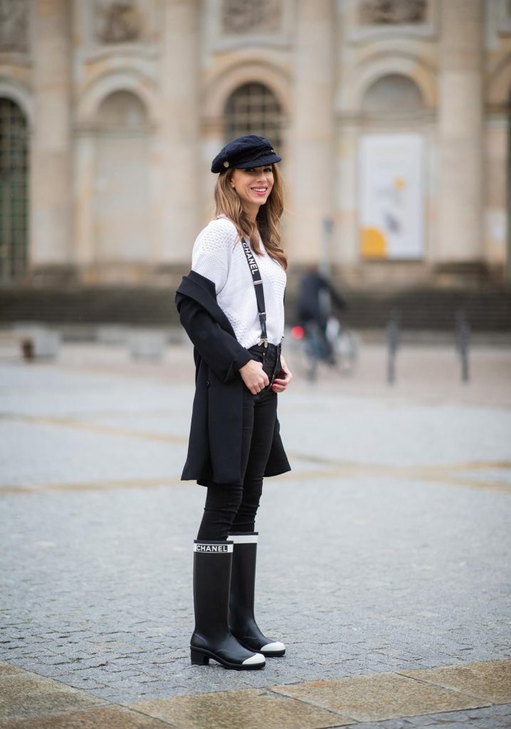 Alexandra Lapp in A Chanel Rain Boots look, wearing a soft long blazer by Steffen Schraut, over a white chunky knit sweater by H&M, black skinny pants with golden buttons by Veronica Beard, styled with Chanel logo suspenders and Chanel rain boots, the Chanel Le boy bag, a Chanel tweed baker boy cap and a transparent umbrella by Mirviory during the Berlin Fashion Week Autumn/Winter 2019 on January 15, 2019 in Berlin, Germany. (Photo by Christian Vierig/Getty Images)