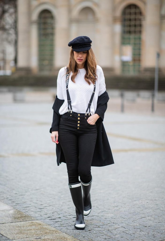 Alexandra Lapp in A Chanel Rain Boots look, wearing a soft long blazer by Steffen Schraut, over a white chunky knit sweater by H&M, black skinny pants with golden buttons by Veronica Beard, styled with Chanel logo suspenders and Chanel rain boots, the Chanel Le boy bag, a Chanel tweed baker boy cap and a transparent umbrella by Mirviory during the Berlin Fashion Week Autumn/Winter 2019 on January 15, 2019 in Berlin, Germany. (Photo by Christian Vierig/Getty Images)