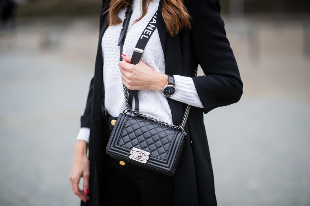 Alexandra Lapp in A Chanel Rain Boots look, wearing a soft long blazer by Steffen Schraut, over a white chunky knit sweater by H&M, black skinny pants with golden buttons by Veronica Beard, styled with Chanel logo suspenders and Chanel rain boots, the Chanel Le boy bag, a Chanel tweed baker boy cap and a transparent umbrella by Mirviory during the Berlin Fashion Week Autumn/Winter 2019 on January 15, 2019 in Berlin, Germany. (Photo by Christian Vierig/Getty Images)
