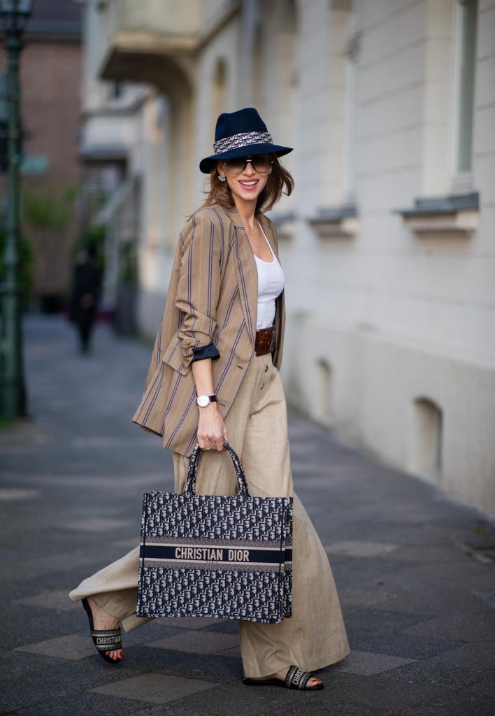 Alexandra Lapp in a Dior Book Tote Bag Look, wearing a beige brown long striped blazer from Zara, white tank top from H&M, waisted belt from Max Mara, high waisted wide leg pants from Staud, Dior Dway mules, Dior Book Tote Dior Oblique bag and a Dior foulard on a blue Borsalino hat on May 04, 2019 in Duesseldorf, Germany. (Photo by Christian Vierig/Getty Images)