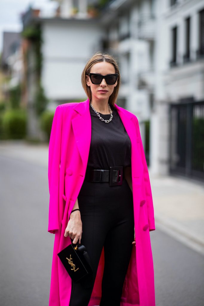 Alexandra Lapp is seen wearing Saint Laurent stretch knit stirrup leggings in black, black oversize t-shirt with shoulder pads from H&M, Dolce Gabbana waist belt in black, Square Knife pumps in neon pink from Balenciaga, double breasted oversize coat and pink blazer from The Attico in pink, Saint Laurent Monogram Clutch in black and Tiffany City HardWear necklace in sterling silver.