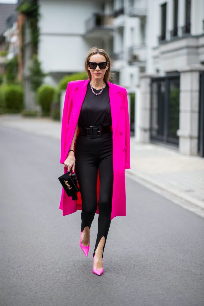 Alexandra Lapp is seen wearing Saint Laurent stretch knit stirrup leggings in black, black oversize t-shirt with shoulder pads from H&M, Dolce Gabbana waist belt in black, Square Knife pumps in neon pink from Balenciaga, double breasted oversize coat and pink blazer from The Attico in pink, Saint Laurent Monogram Clutch in black and Tiffany City HardWear necklace in sterling silver.