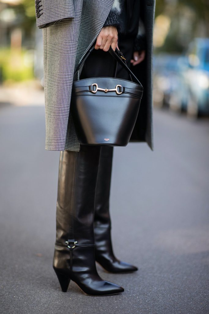 Alexandra Lapp is seen wearing Alexander McQueen coat with prince of wales check, SAINT LAURENT striped mohair-blend sweater, SAINT LAURENT high waist pants in black, CELINE Bucket Crécy bag in black and Isabel Marant pointed-toe knee-high autumn boots in black. All looks by Breuninger.