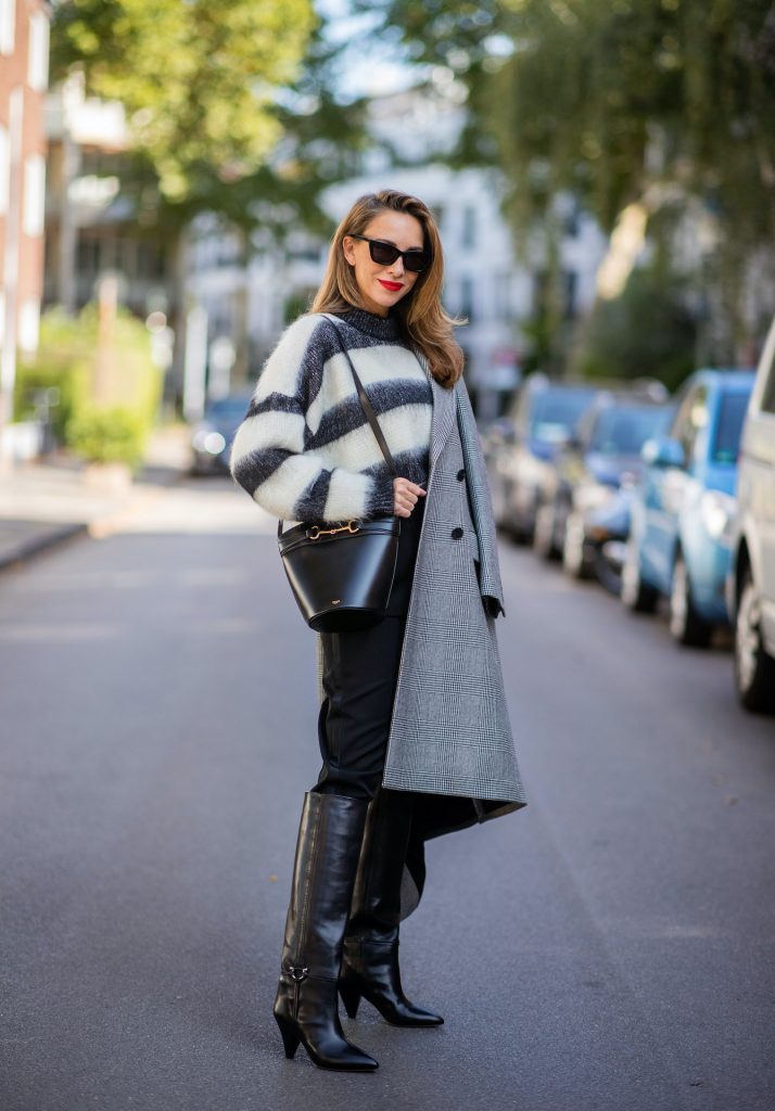 Alexandra Lapp is seen wearing Alexander McQueen coat with prince of wales check, SAINT LAURENT striped mohair-blend sweater, SAINT LAURENT high waist pants in black, CELINE Bucket Crécy bag in black and Isabel Marant pointed-toe knee-high autumn boots in black. All looks by Breuninger.