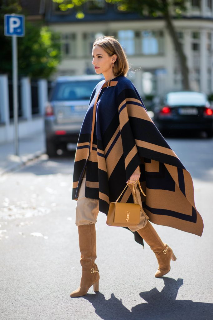 Alexandra Lapp is seen wearing Chloé striped wool cape, Chloé chunky-knit sleeveless jumper in camel, Chloé linen cargo pants in beige, SAINT LAURENT Kate medium bag in camel and CELINE Claude calfskin autumn boots in sand. All looks by Breuninger.