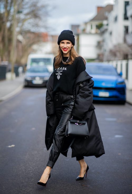 Alexandra Lapp is seen wearing PRADA Piumino nylon coat in black, PRADA knitted logo jumper in black, TIFFANY&CO. City HardWear necklace in sterling silver, SET leather joggers in black, XX knitted beanie, HERMÈS Kelly 28 bag in black, CHRISTIAN LOUBOUTIN So Kate pumps in black.