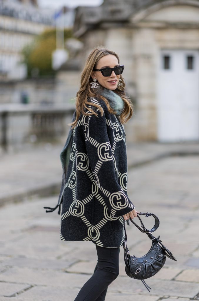Alexandra Lapp is seen wearing GUCCI reversible cardigan in black and ecru, BALMAIN pants in black, ACNE STUDIOS scarf in green and grey, BALENCIAGA Le Cagole bag in black, BALENCIAGA ankle boots Cagole in black, CELINE cat eye sunglasses in silver, and Chanel ear rings in black. 